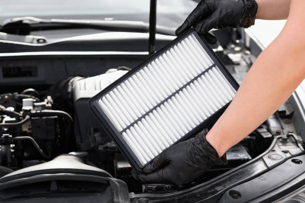 istock Replacing the air filter in a car. Auto mechanic in gray gloves holds an engine air filter against the engine compartment. Concept of maintenance, ecology, car care, auto parts 2179772149