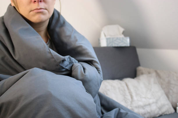 istock Sick woman sitting on sofa with grey blanket, blurry background with tissue box 2179783111
