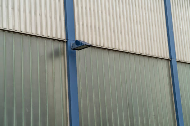 Single blue security light is mounted on the exterior wall of a modern industrial building, casting light onto the corrugated metal and translucent panels