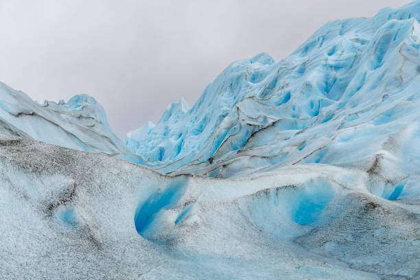 Portrait of a young adult man on Perito Moreno Glacier. He's looking at camera and smiling. He's standing on the glacier with snowshoes and helmet.