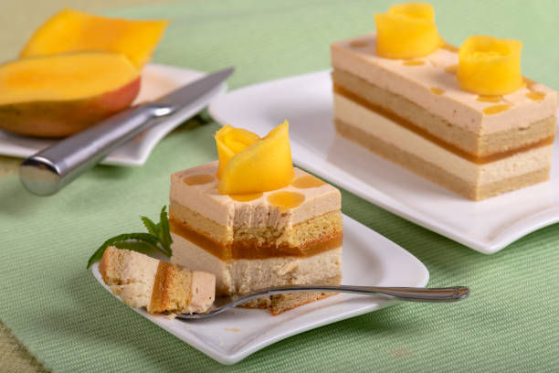 Home made mango cake with mango cream decorated with slices of mango. The cake is on a plate on the table with a checkered tablecloth. It ready to eat.