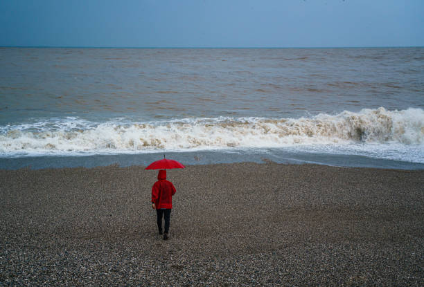istock Lonely man walking on the beach on a rainy day 2179816490