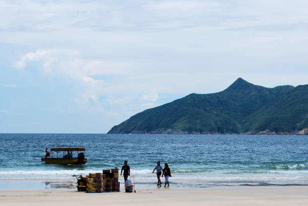 This image from September 2010 was captured at a beach called Sai Wan, which belongs to the Sai Kung Peninsula in Hong Kong. The beach is also called Tai Long Sai Wan, in order to distinguish it from other beaches and bays of the same name. The scene in the photograph appears to depict some sort of provisional delivery that has just been unloaded from a small boat. The people in the image appear to be mostly locals, or at least local to the surrounding area.
