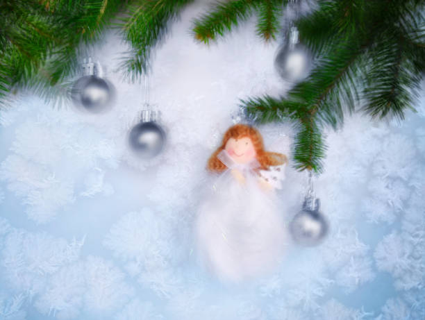 Christmas fairy doll against the background of frozen window and New Year tree branches decorated with silver balls. Intentional camera movement.