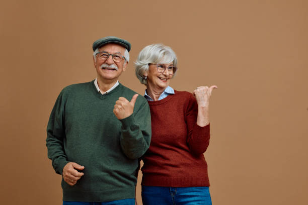 istock Happy senior couple pointing to the side while standing against neutral background. 2179832326