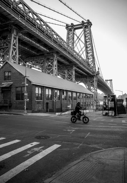 New York City, USA - November 19, 2023: \nA man passes under the Manhattan Bridge on a bicycle. black and white composition