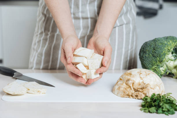 Person Holding Cubed Celeriac in Kitchen Close-up of a person holding cubed celeriac on a cutting board, demonstrate cutting technic of celeriac for cooking prep Celeriac stock pictures, royalty-free photos & images