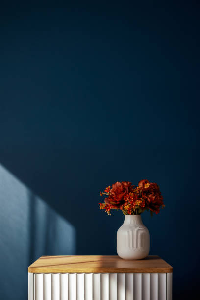 istock Minimalist interior with a white vase and red flowers on a ribbed bedside table against a deep blue wall 2179846801