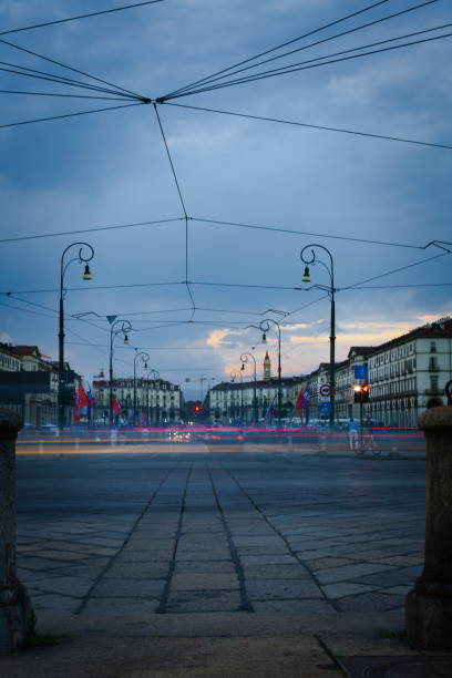 An atmospheric evening scene in Turin, Italy, showcasing the elegant illuminated streets near the Po River. The cobbled tram tracks and vintage streetlights create a nostalgic ambiance, while historic buildings glow softly under the twilight sky. A perfect capture of the charm and tranquility of Turin's cityscape.
