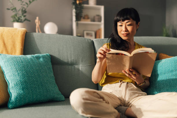 istock Asian woman reading book while relaxing on a green comfortable sofa. 2179848993