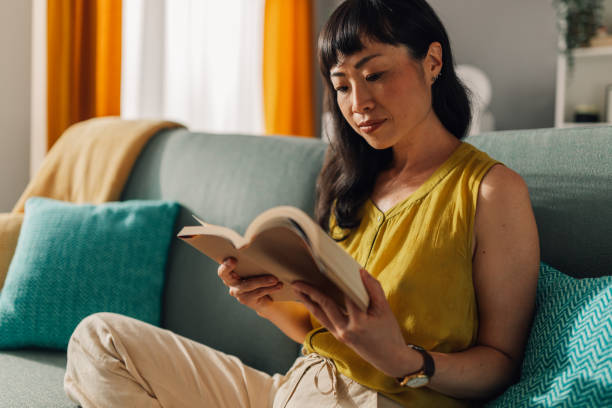 istock Concentrated asian woman reading a book on a sofa 2179849003