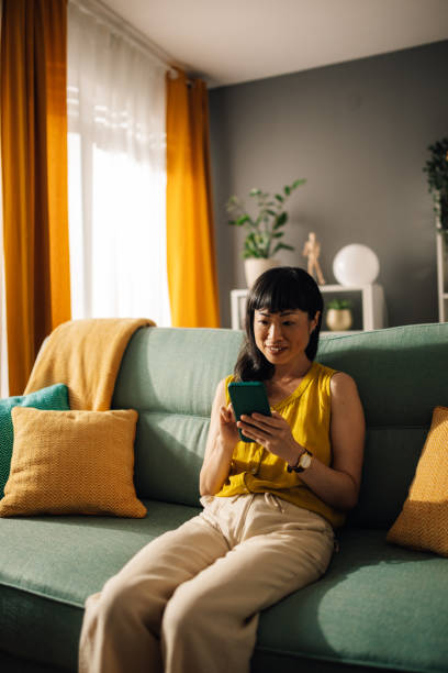istock Asian woman in cheerful mood using smartphone on modern green couch 2179849006