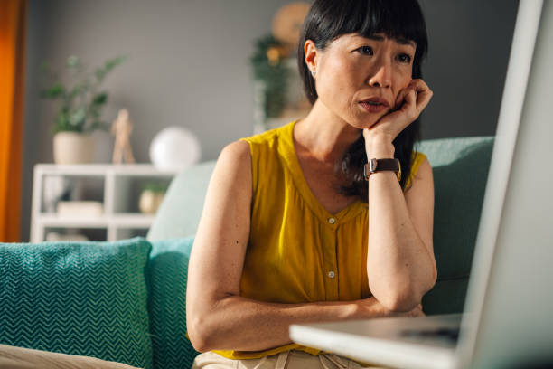 istock Thoughtful asian woman leaning on hand while looking at laptop screen 2179849064