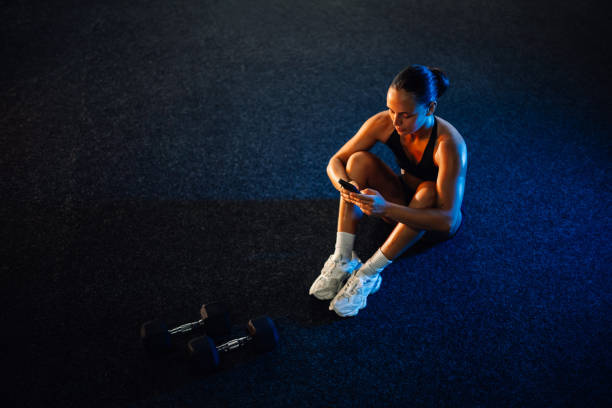 istock Young athletic woman using smartphone app after training with dumbbells 2179850164