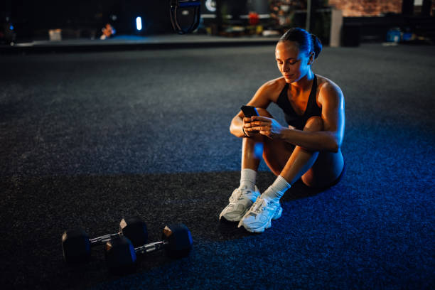 istock Sportswoman using smartphone sitting on gym floor 2179850220