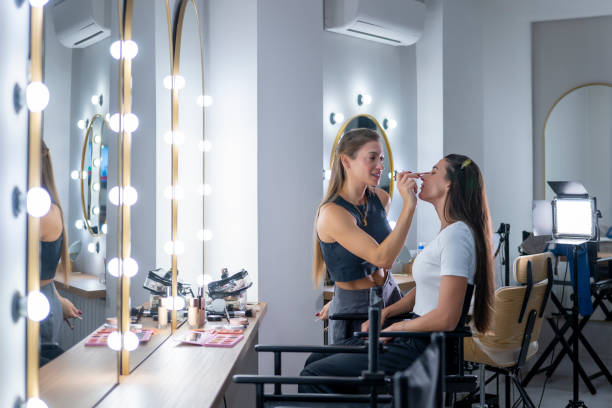 istock Makeup artist applies eyeshadow to model in a bright studio surrounded by mirrors and vanity lights. 2179861757