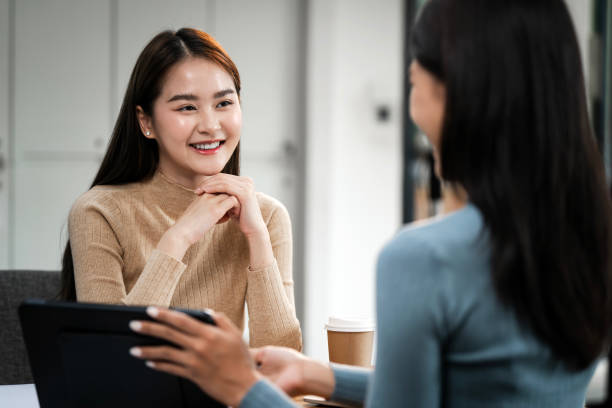 istock Two asian business women sitting at desk using tablet and talking about analyzing documents in workplace office 2179864721