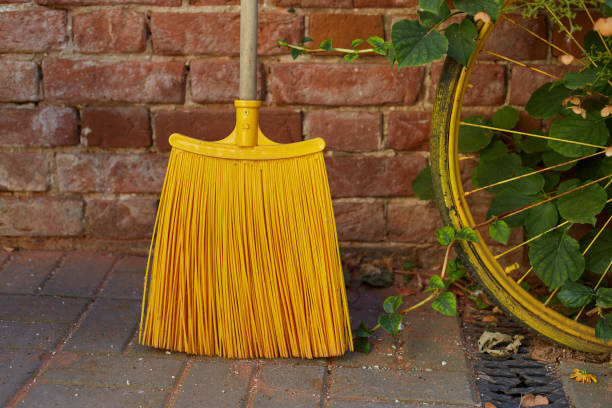 Yellow broom and dustpan leaning against the red brick wall at the corner of a house patio.