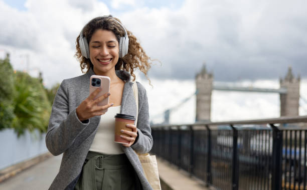 istock Happy woman walking by Tower Bridge in London and using her cell phone while drinking coffee on the go 2179891820