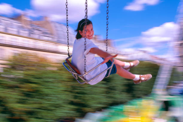 Craziness and freedom. Young summer girl playing on swing-set outdoor. Crazy playful child swinging very high to touch the sky.