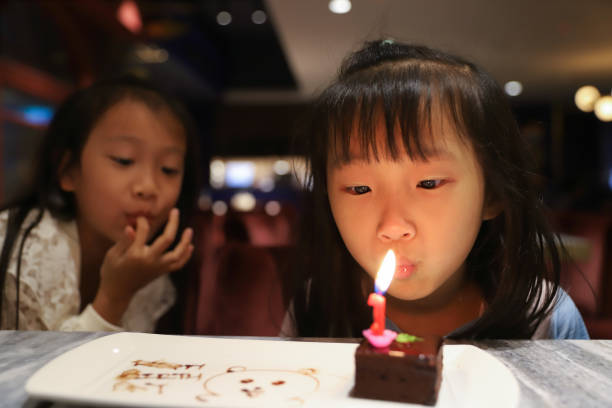 two girls eating cake in restaurant. Blowing candles to celebrate birthday, restaurant with atmospheric lights, full of warm colors