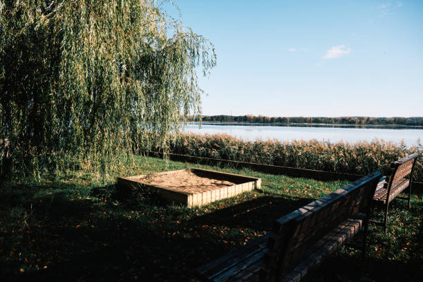 Sandbox under willow tree on embankment in sunlit autumn town
