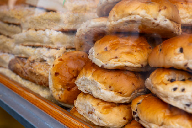 Close-up of a display of freshly baked buns in a bakery window. The buns are arranged in a stack and are golden brown in color. Some of the buns have visible chocolate chips.