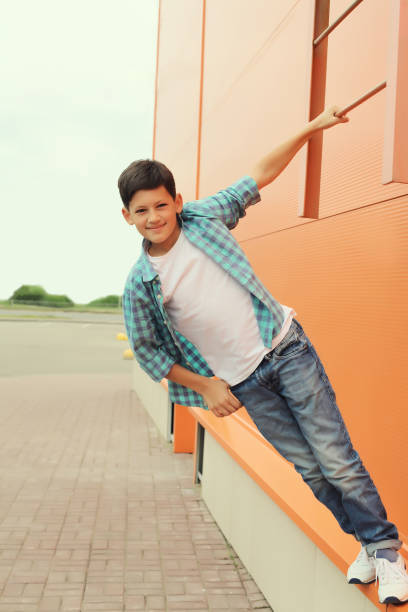 Happy smiling teenager boy in casual clothing in the city, orange wall background stock photo