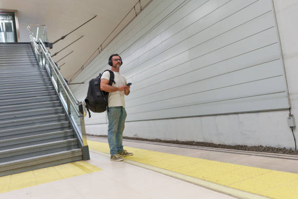 Middle-Aged Man in Casual Clothing with Backpack Using Smartphone for E-Ticket While Waiting for Train at Station