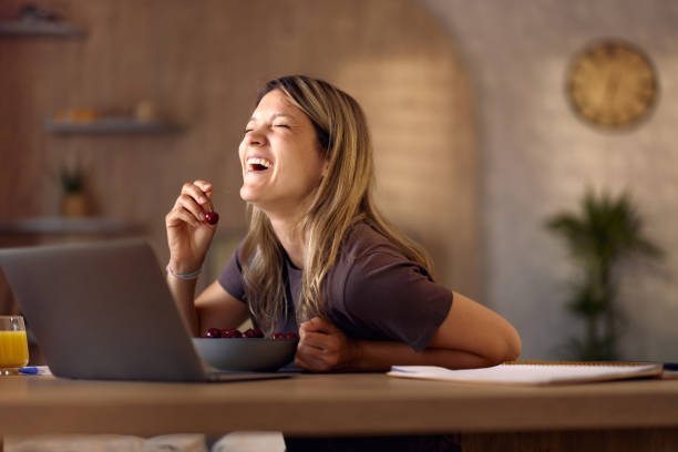 istock Cheerful woman eating cherry while using laptop at home. 2179928035