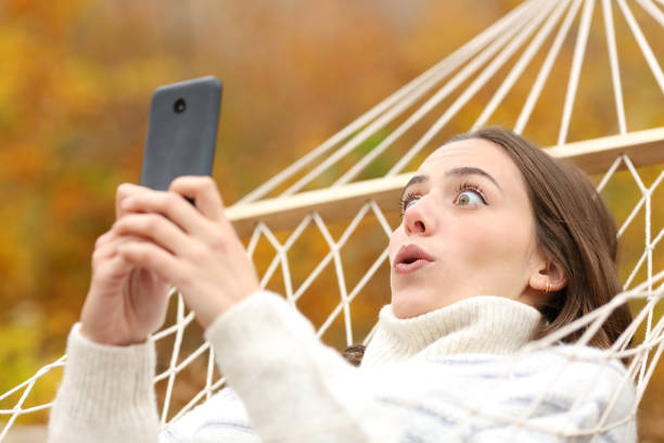 istock Amazed woman in autumn checking phone on a hammock 2179929871