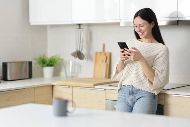 istock Happy asian woman standing in the kitchen using phone 2179931190