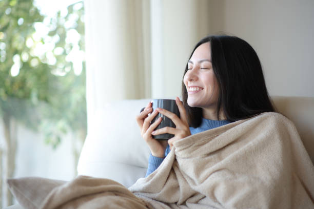 Happy asian woman heating drinking coffee covered with blanket stock photo