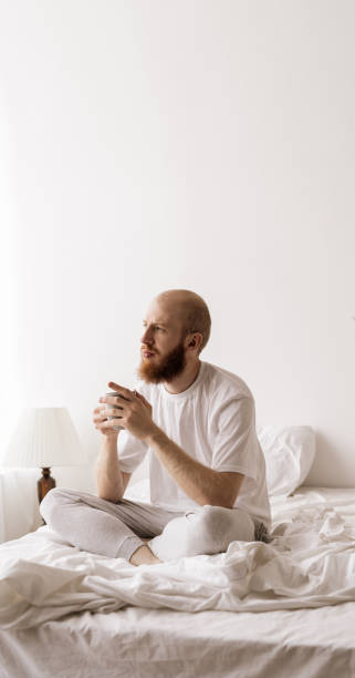 istock young bearded man smiling and drinking tea or coffee on bed in white bedroom. Vertical banner. 2179932191