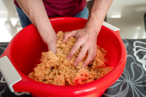 Close-up image of hands kneading the almond-based dough for panellets in a red mixing bowl, as part of the traditional preparation for the Castanyada celebration in Catalonia. The image highlights the homemade, artisanal process of making this iconic dessert, central to Catalan culture during the holiday season.