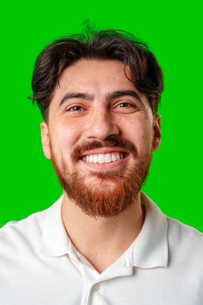 istock A smiling young man with a beard poses against a bright green background 2179939044