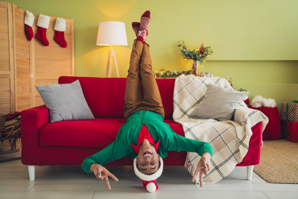 Photo of cheerful positive guy dressed green pullover showing v-signs enjoying x-mas eve indoors house apartment room Photo of cheerful positive guy dressed green pullover showing v-signs enjoying x-mas eve indoors house apartment room. black hat upside down stock pictures, royalty-free photos & images