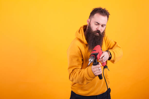 istock Bearded handyman in yellow hoodie holding power drill over yellow background. 2179947607
