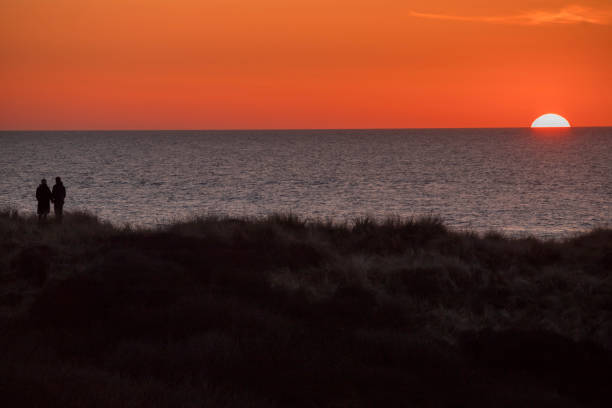 A couple looks at the sun setting in the ocean