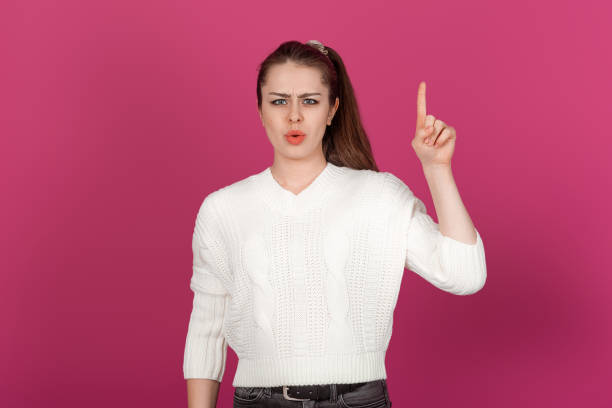 istock Displeased Young Woman Pointing Upward with a Serious Expression. Standing Against a Bright Background, Her Facial Expression Indicate Frustration and Discontent 2179953794