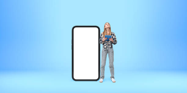 istock Woman holding tablet standing next to large smartphone mockup on 2179956040