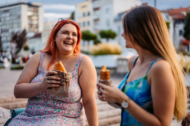 istock Two Female Friends Eating A Pastry While Sitting In The Park 2179959536