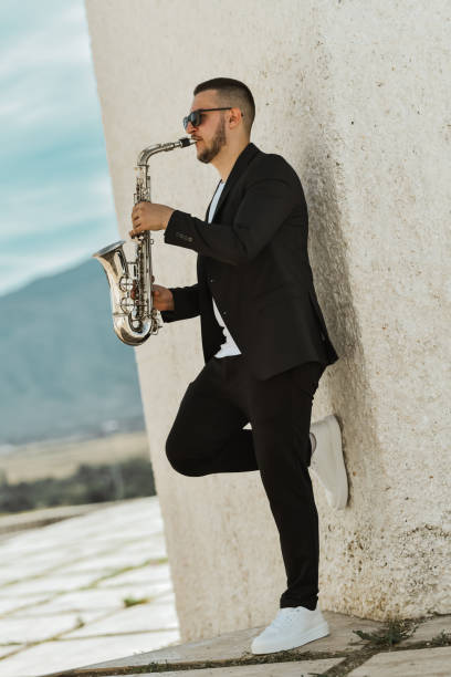 istock Young Male Saxophonist Leaning on Wall While Playing His Saxophone and Creating Magical Melodies 2179960483