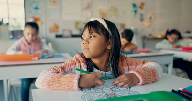 istock Thinking, child and girl drawing in classroom with notebook, growth and development in education. Study, desk and kid with color pencil, stationery and creative learning ideas at elementary school 2179961137
