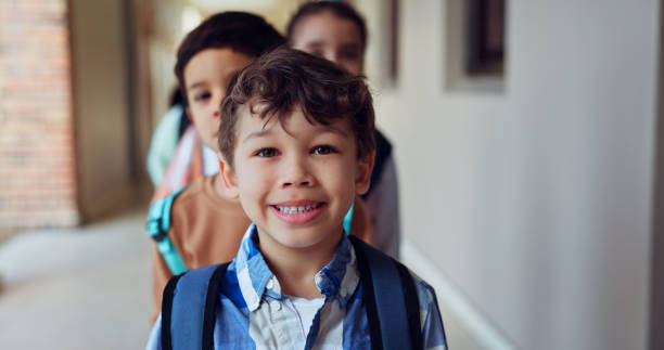 istock Hallway, portrait and boy with students, school and education with happiness, smile and learning. Lobby, face and kids with knowledge, child development and friends with bonding, joy and cheerful 2179961159