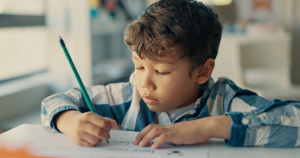 Boy, child and writing with paper in classroom for education, learning and assessment for progress at academy. Kid, quiz and activity for development, scholarship and thinking with language at school