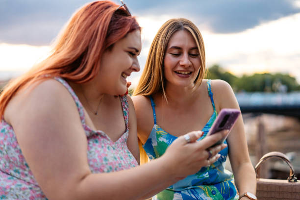 istock Two Female Friends Using Smart Phone While Sitting In The Park 2179961909
