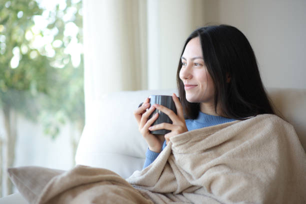 istock Relaxed asian woman looking through a window keeping warm 2179965528
