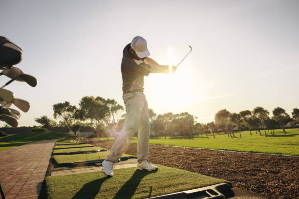 Professional golfer practicing his swing in the sunlight at a beautiful golf course Captured in the midst of a powerful swing, a professional golfer practices under the brilliant sun on a serene golf course. Man hitting a shot at a golf driving range. golfer swinging club stock pictures, royalty-free photos & images