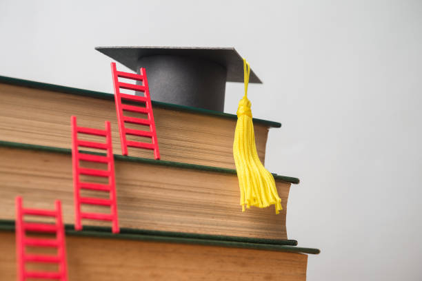Graduation cap on textbooks with red ladder with white wall background.